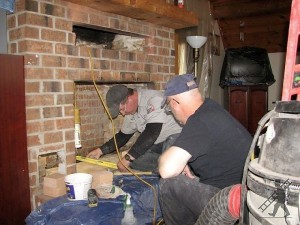 Two Men working on chimney they are surrounded by materials and taking measurments of the chimney