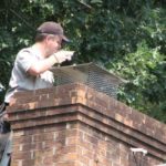 Man inspecting chimney on roof wearing a black hat and gloves