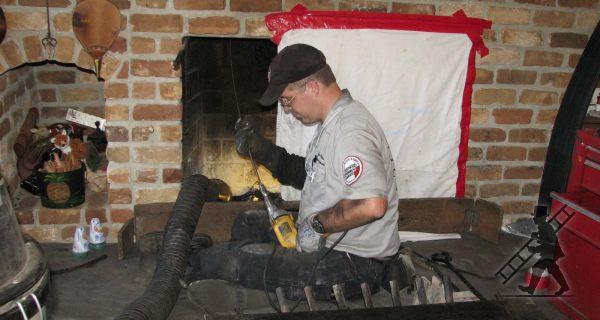 Man in grey work shirt and black hat cleaning fireplace. Surrounded by tools